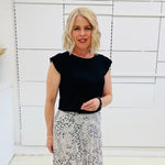 Woman wearing a black top and patterned skirt against a white background