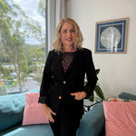 Woman in a black suit standing in a living room with a couch and framed picture on the wall.