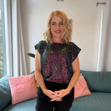 Woman wearing a sequin top sitting on a couch in a living room.