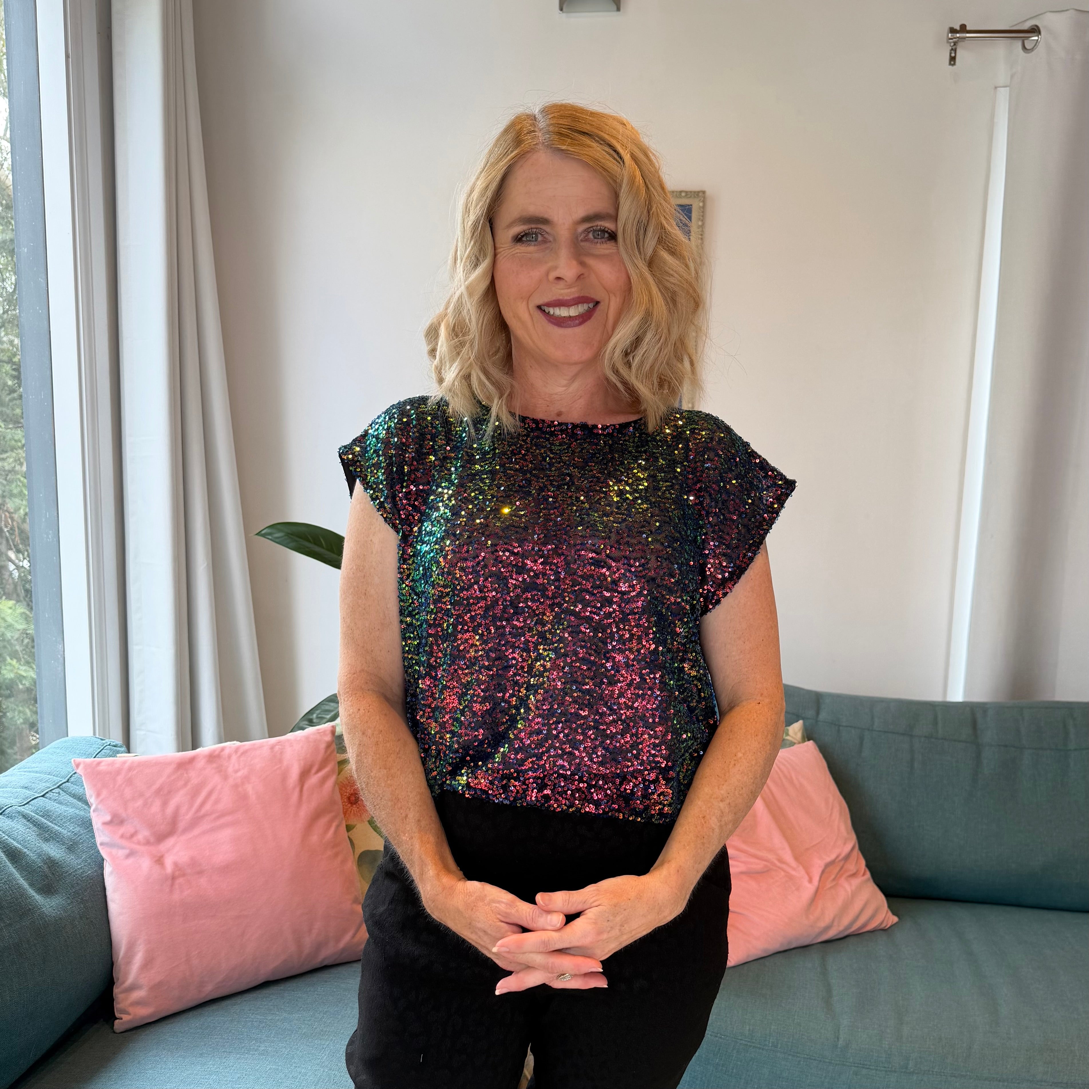 Woman wearing a sequin top sitting on a couch in a living room.