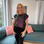 Woman standing in a living room with a blue couch and pink pillows.