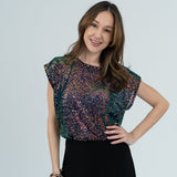 Model in sparkly top in black skirt in white room.