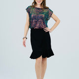 A woman modeling a two-piece outfit consisting of a short-sleeve top with a multicolor floral sequin pattern and a black flared skirt, photographed against a light gray studio background.