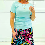 Woman wearing a light blue top and colorful skirt against a white background