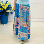 Person wearing a colorful patterned skirt with a blue pot of flowers in the background.