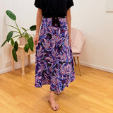 Person wearing a colorful patterned skirt in a room with a plant and chair.