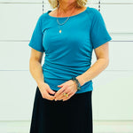 Person wearing a teal coloured dressy  top and black skirt against a white background.