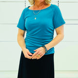 Person wearing a teal coloured dressy  top and black skirt against a white background.