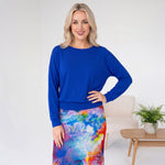 Woman wearing a blue top and colorful skirt in a minimalistic room.