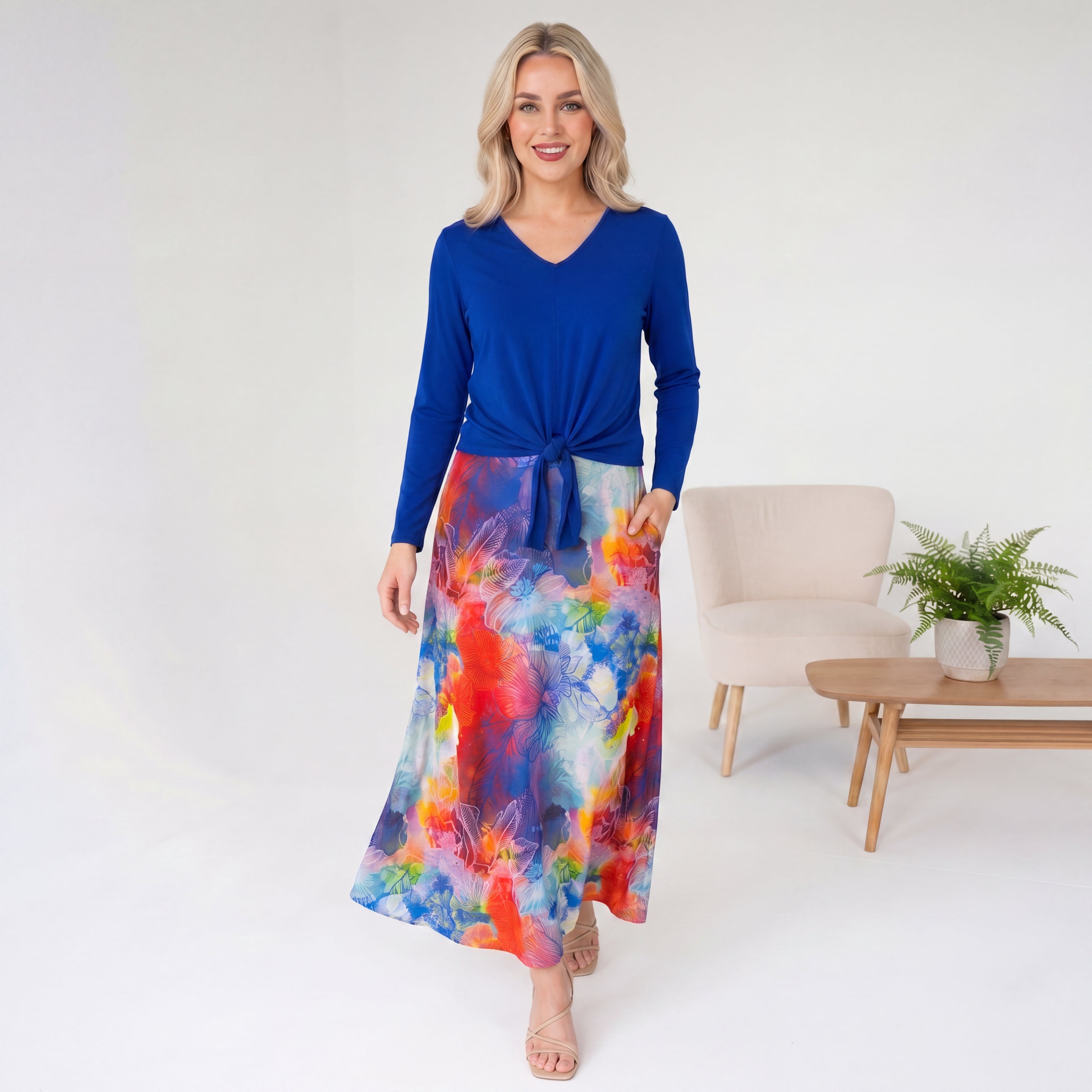 Woman wearing a blue top and colorful skirt in a minimalistic room.