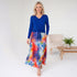 Woman wearing a blue top and colorful skirt in a minimalistic room.
