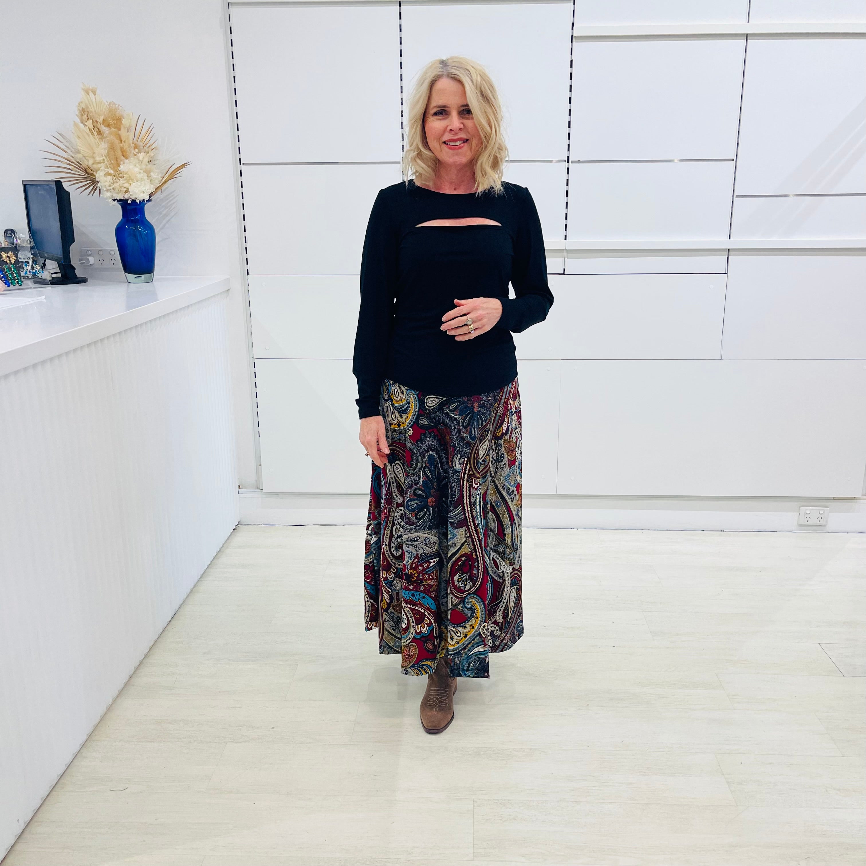 Woman wearing a black top and patterned skirt standing in a room with white walls.