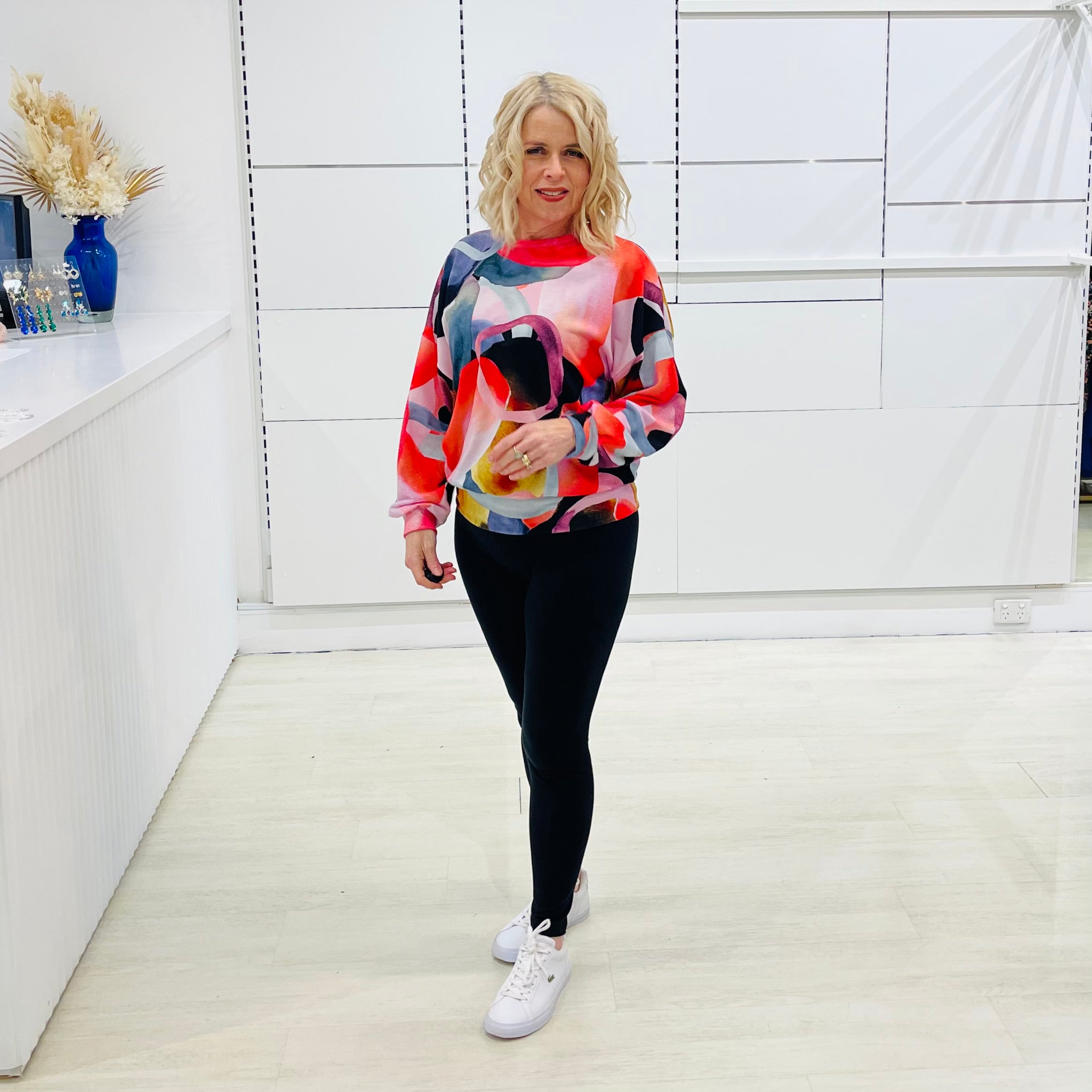 Woman wearing a colorful sweater and black leggings in a white fashion studio.