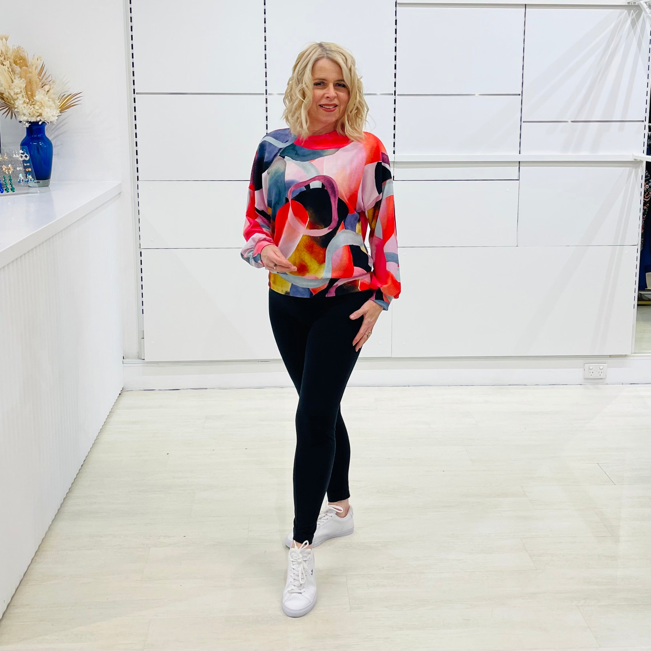 Woman wearing a colorful sweater and black pants in a minimalistic room.