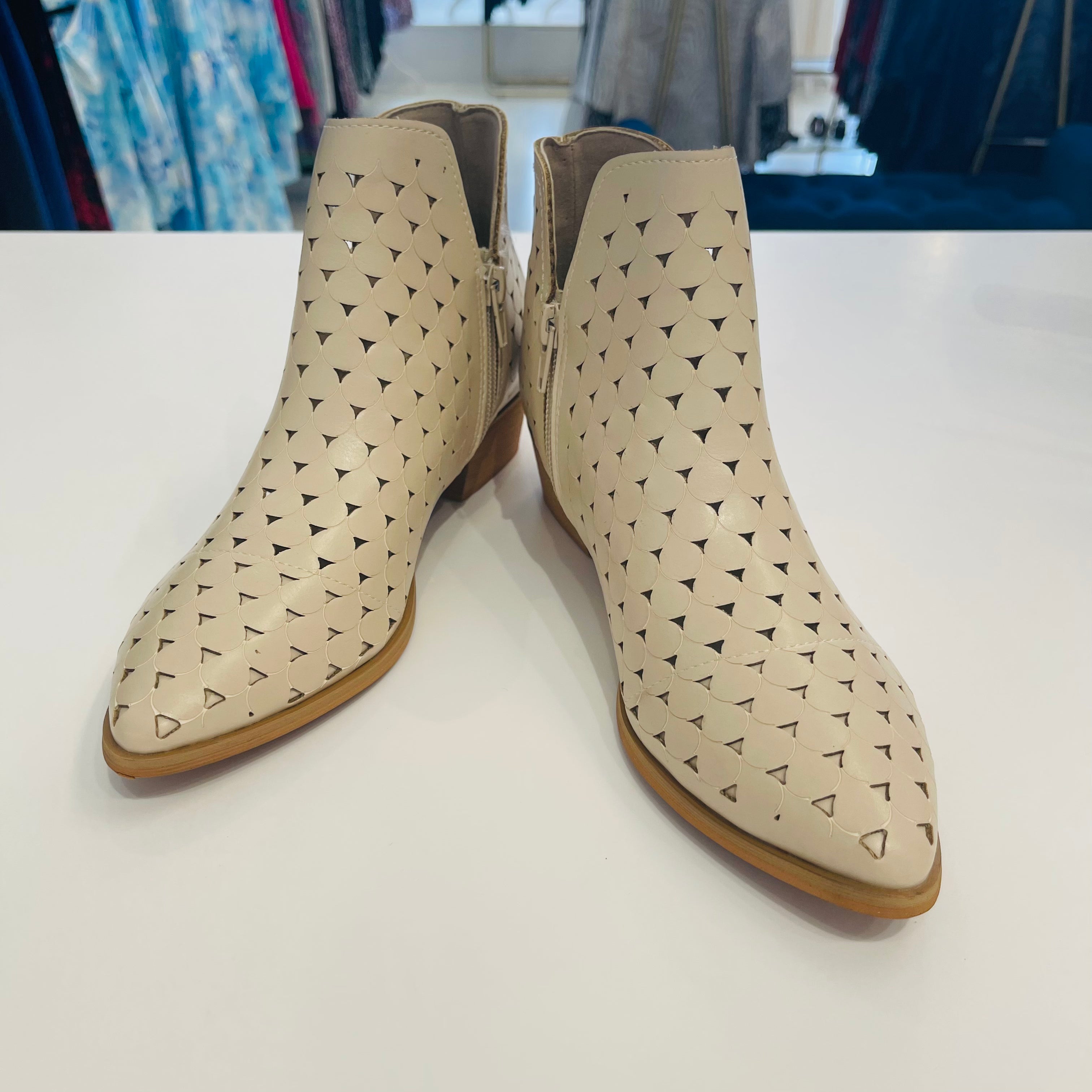 Intricate cut out design on cream colored man made leather ankle boots.
