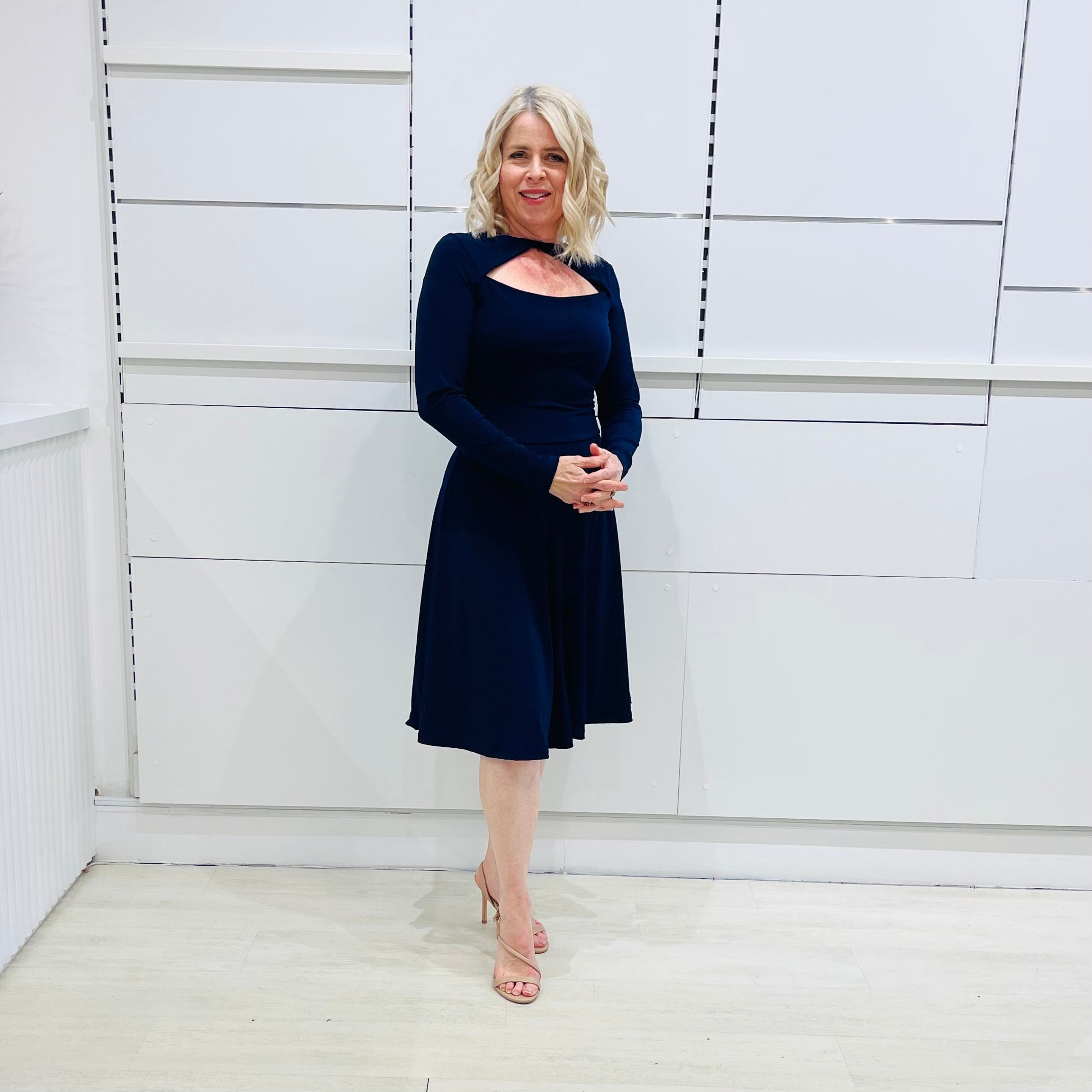 Side view, Penelope dress in deep navy blue, worn by model- elegant long sleeve design, knee length, with modern neckline.