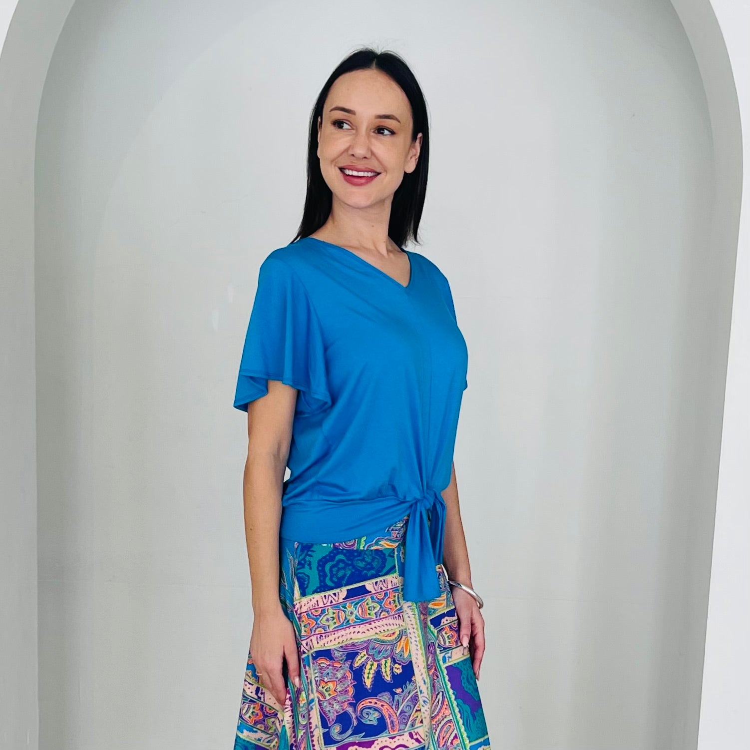 Woman wearing a blue top and colorful patterned skirt against a white background