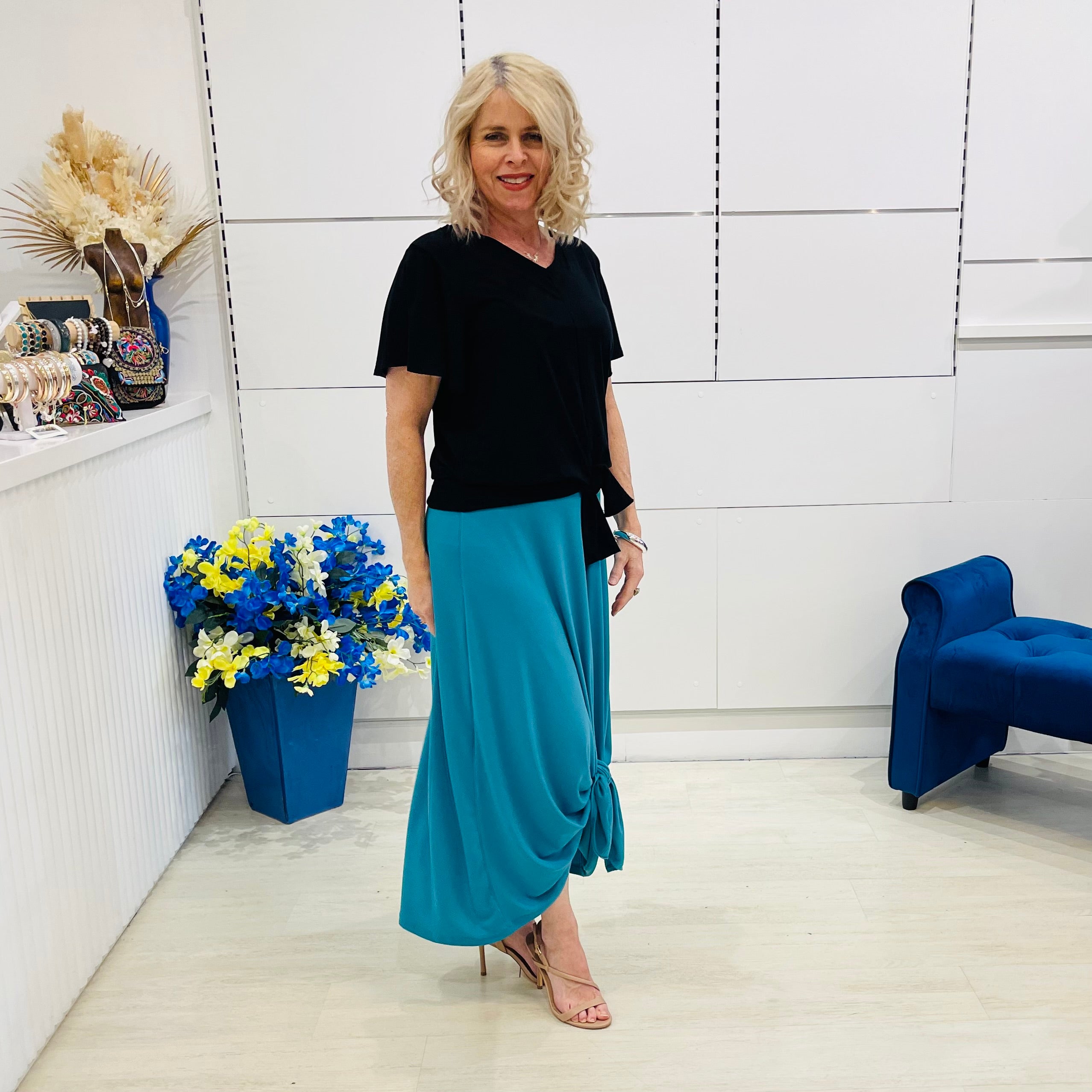 Woman in black top and blue skirt standing in a modern room with white walls and blue accents.