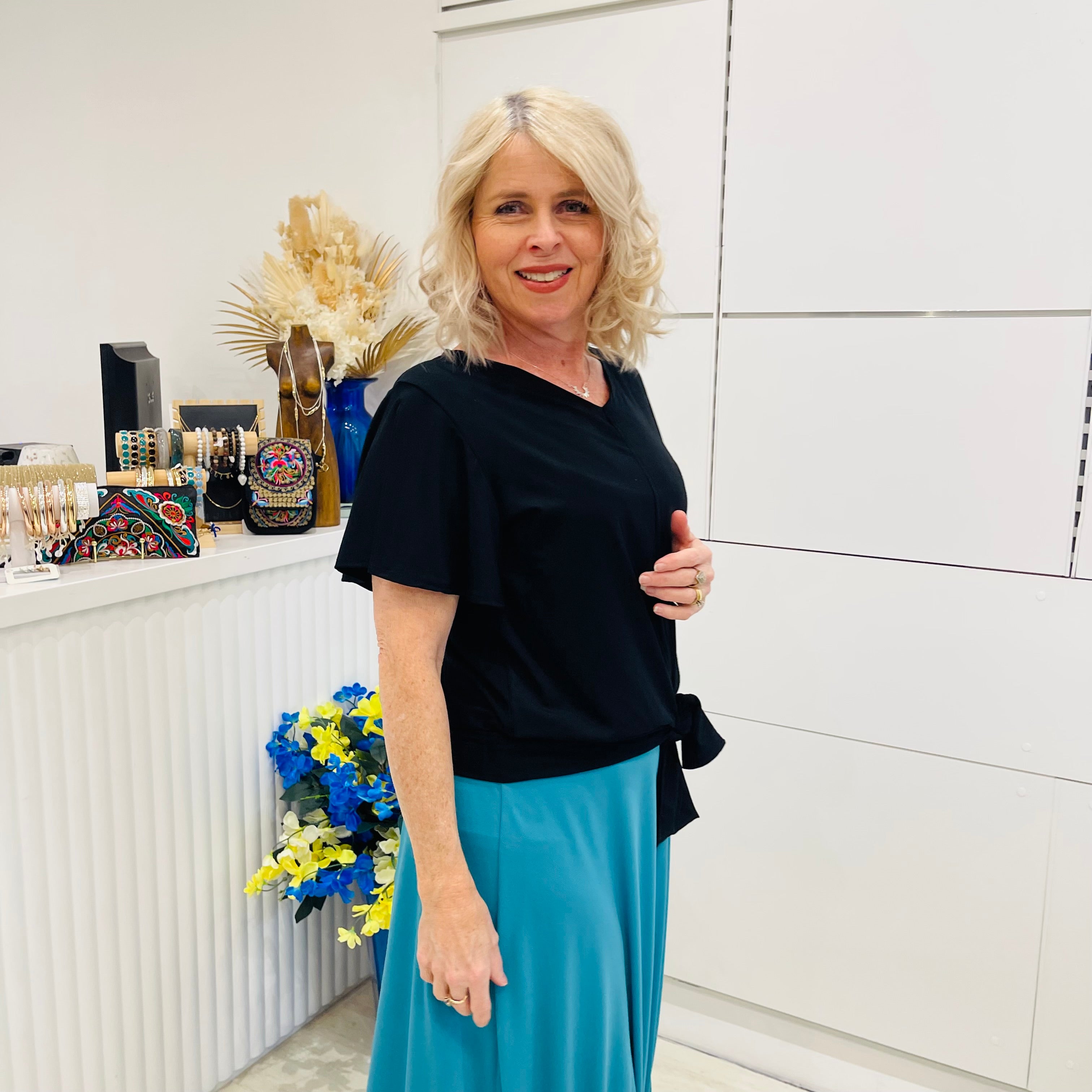 Woman in black top and blue skirt standing in a room with decorative items.