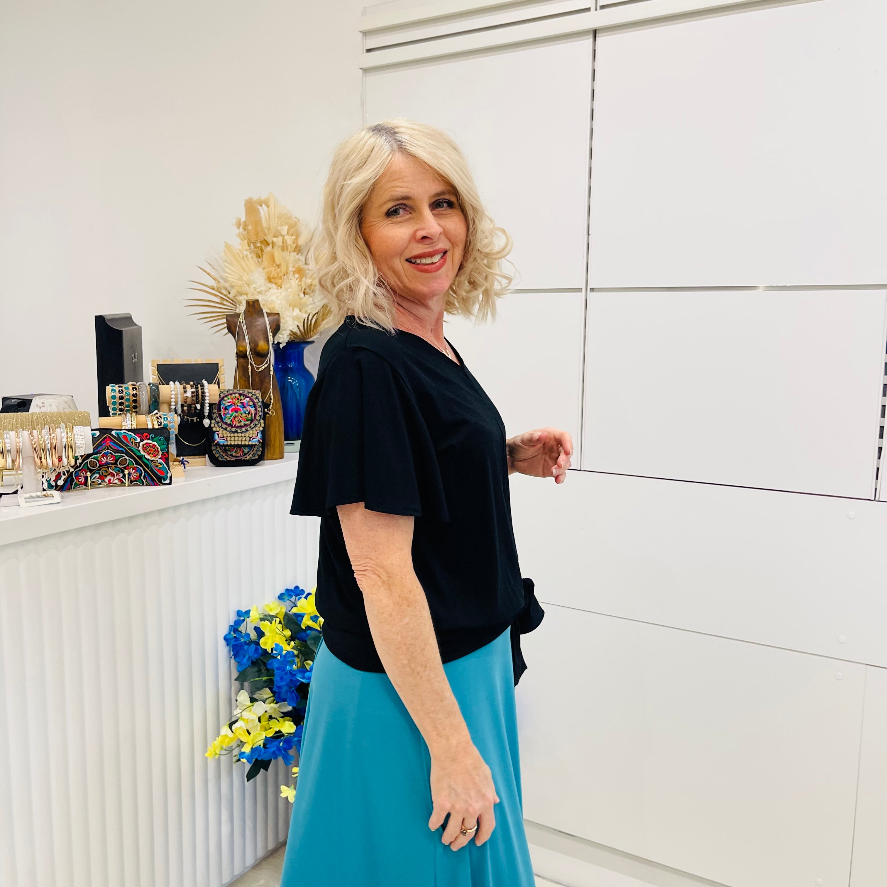 Woman in a black top and blue skirt standing in a room with decorative items.