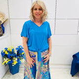 Woman wearing a blue top and colorful skirt standing in a room with white walls and decorative elements.
