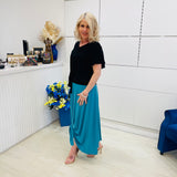 Woman in black top and blue skirt standing in a room with white walls and a blue chair.