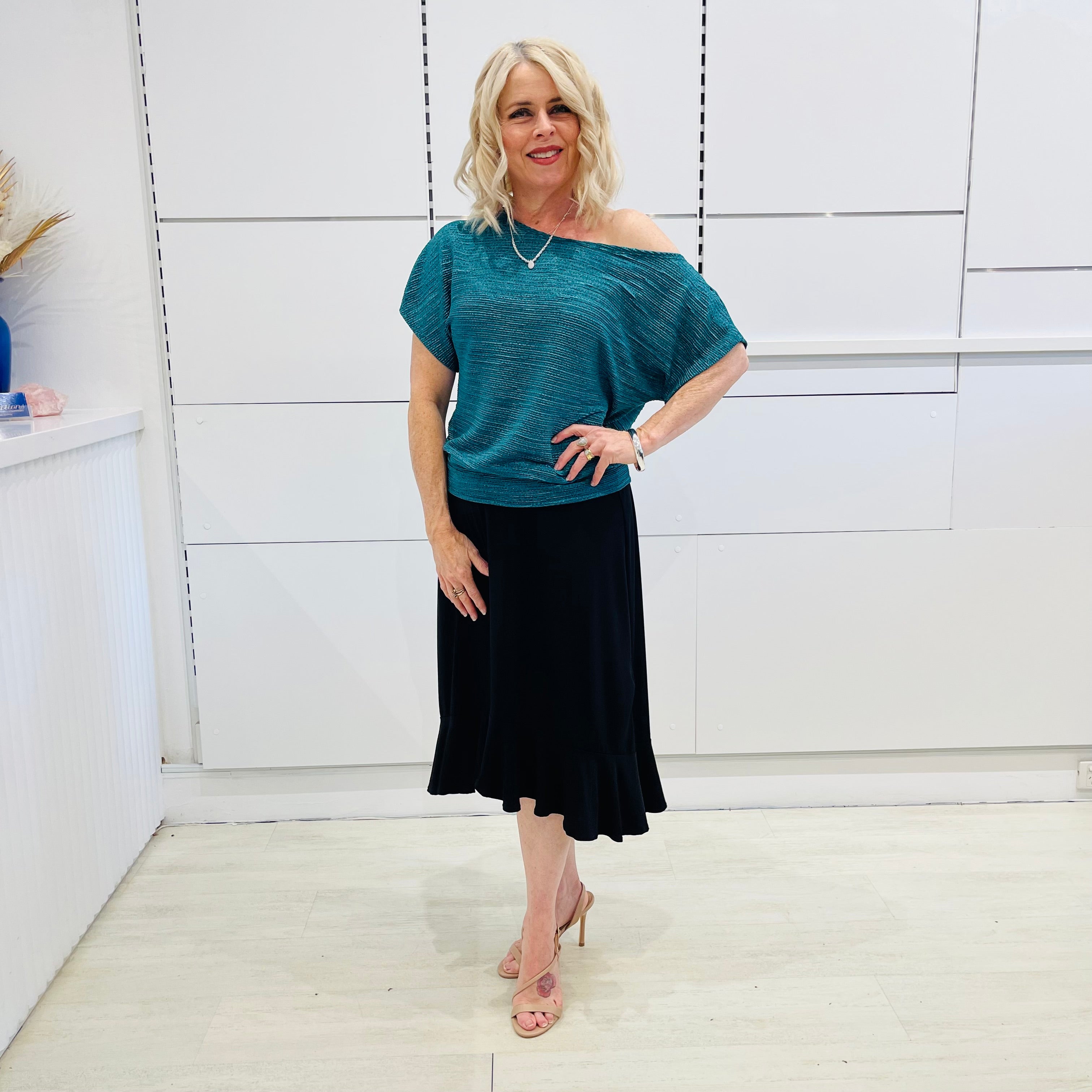 Stunning off the shoulder emerald green top with delicate shimmer. Flattering relaxed fit cut with stretch waistband for style and fit. Worn with black stretch skirt with asymmetrical hemline small ruffle detail.