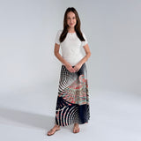 Woman wearing a white top and a long, patterned skirt on a plain background