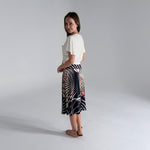 Woman wearing a white top and patterned skirt on a plain background