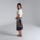 Woman wearing a white top and patterned skirt on a plain background