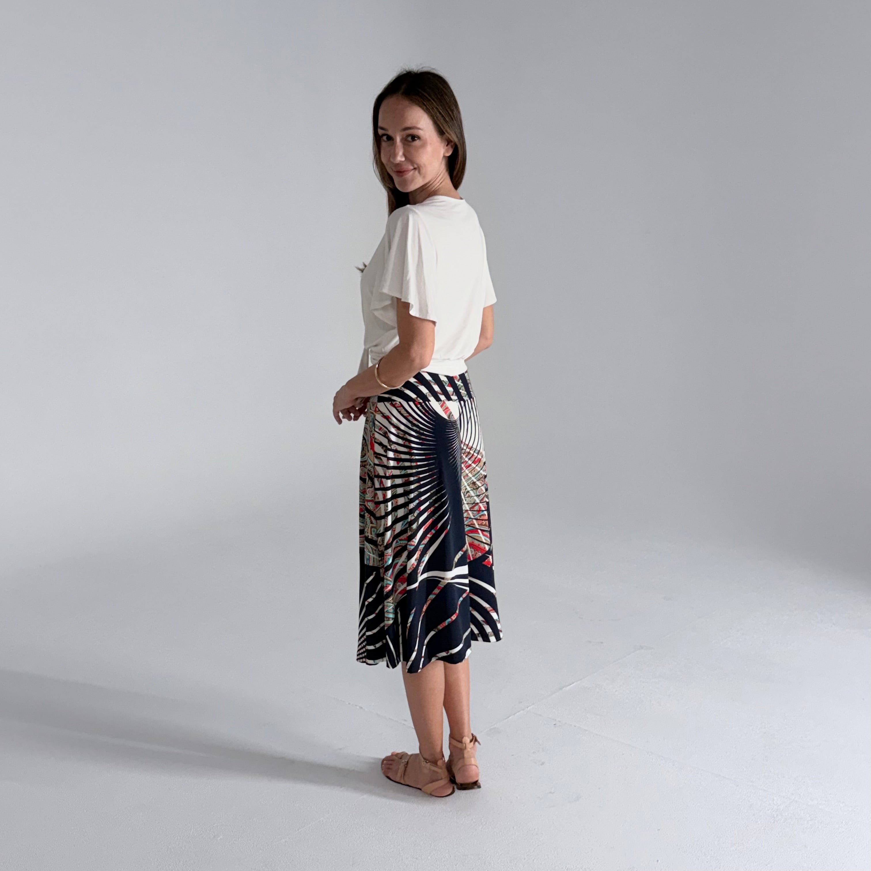Woman wearing a white top and patterned skirt on a plain background