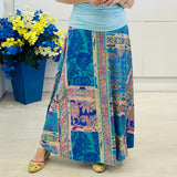 Person wearing a colorful patterned skirt with a blue pot of flowers in the background.