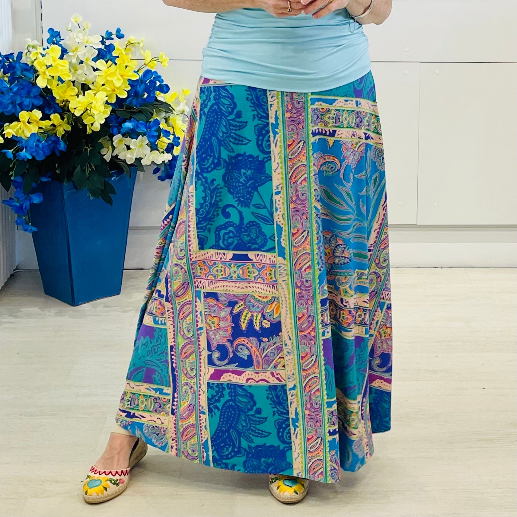 Person wearing a colorful patterned skirt with a blue pot of flowers in the background.