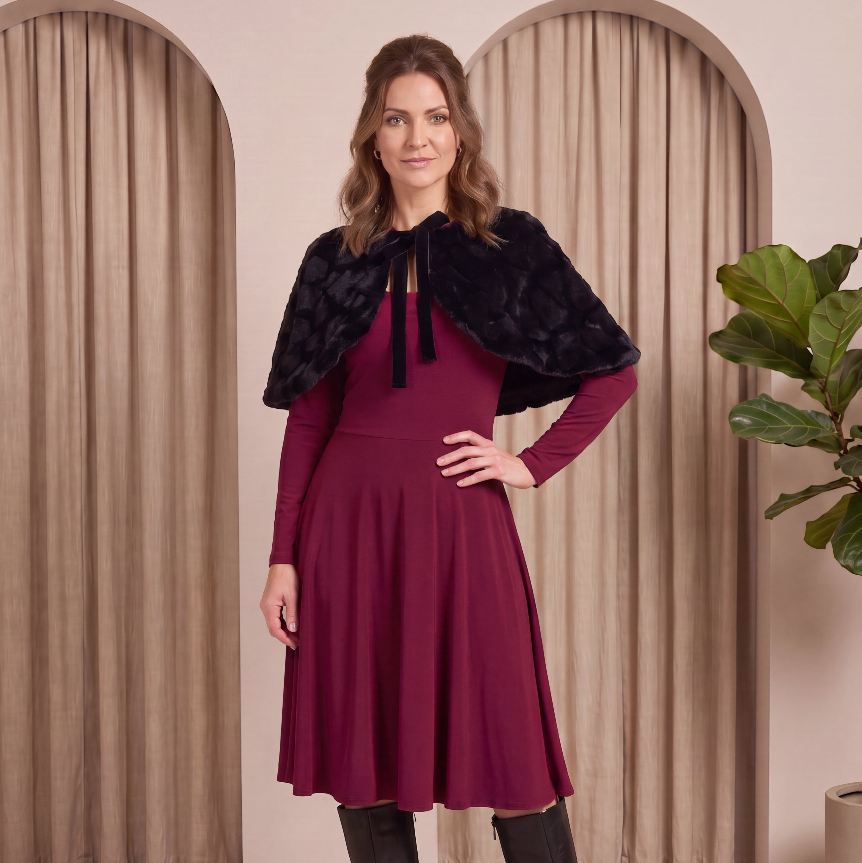 Woman wearing a burgundy dress with a black fur shrug in a neutral setting