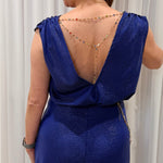 A woman shown from the back wearing a metallic royal blue sleeveless dress with a deep open back, decorated with a delicate beaded gold chain draped across her upper back.