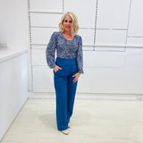 Woman wearing a long sleeve, semi fitted, flowy blue top with a delicate leaf print, paired with denim blue colored linen pants.