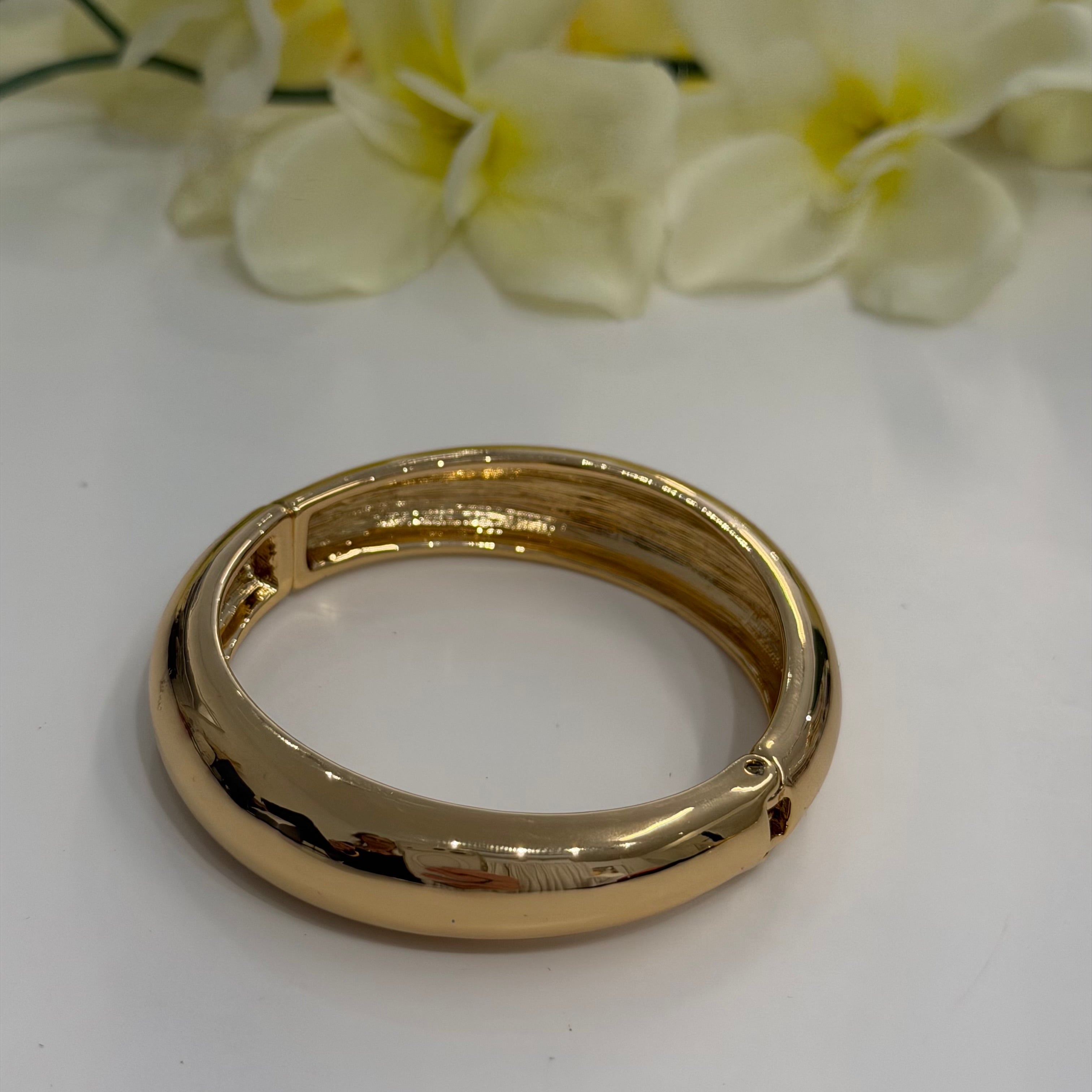 Gold bracelet on a white surface with yellow flowers in the background