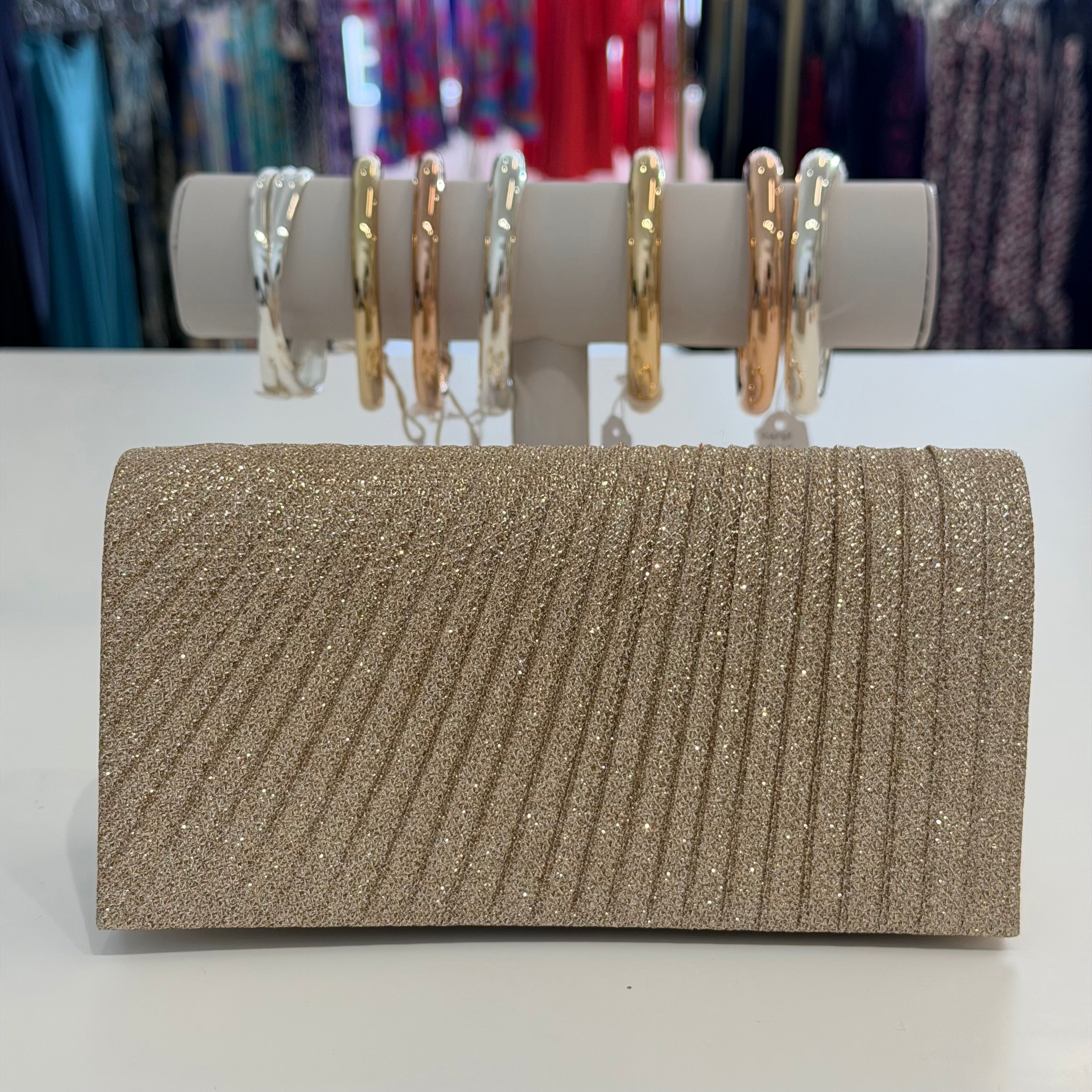 Sparkly clutch bag on a white surface with jewelry in the background