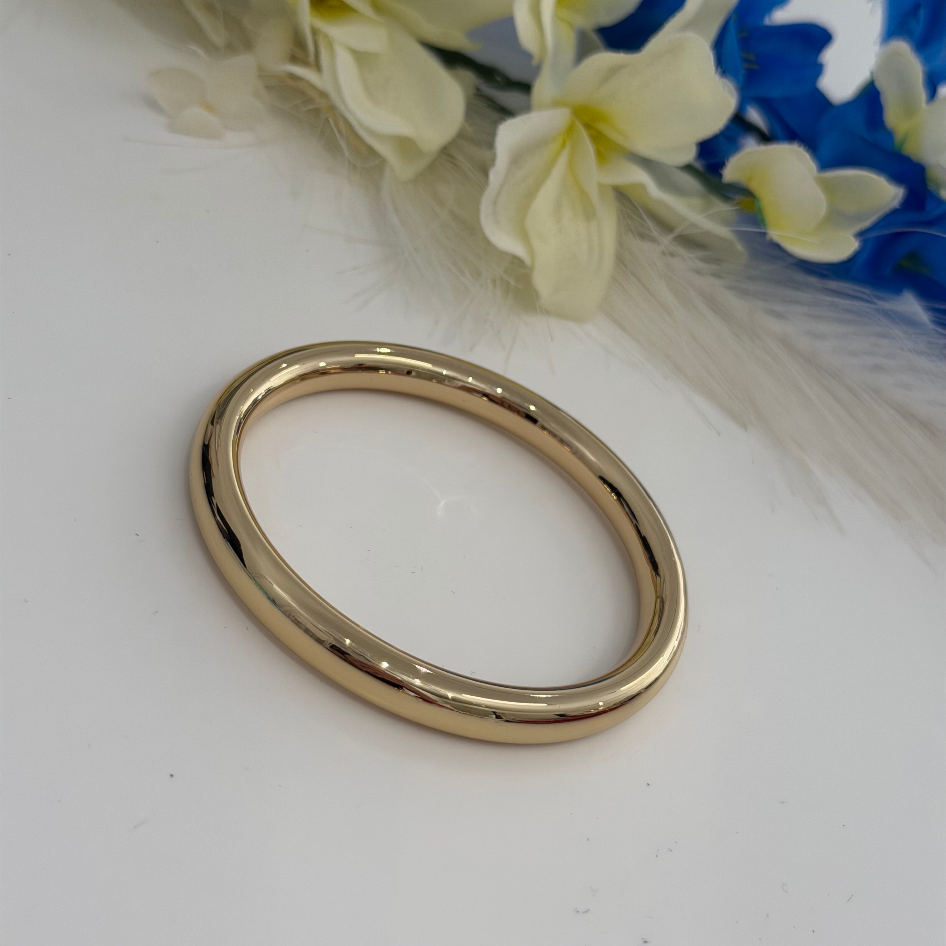 Gold bangle on a white surface with flowers in the background