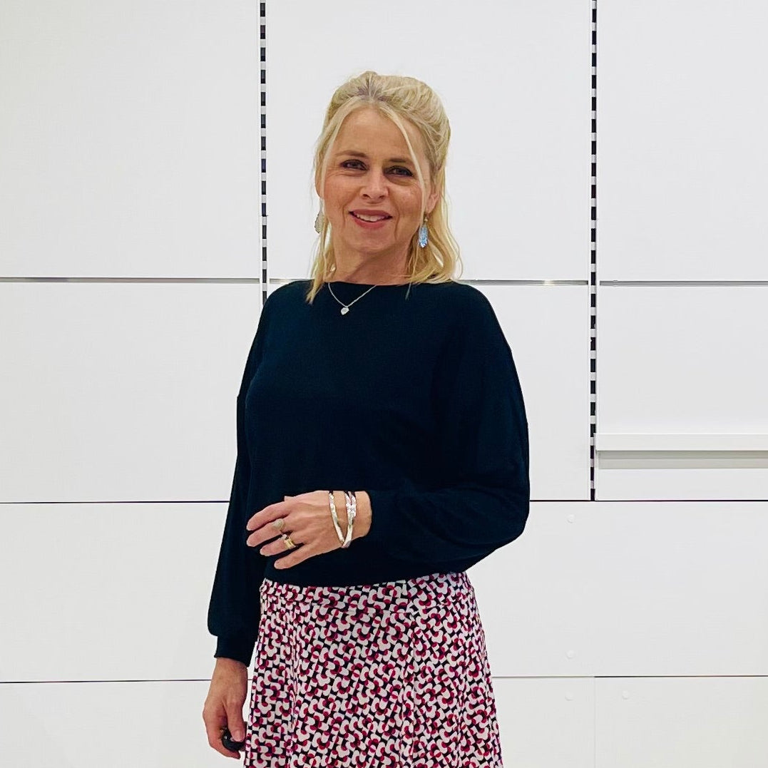 Woman in black top and printed skirt standing in a white room 