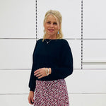 Woman in black top and printed skirt standing in a white room 