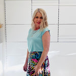 Woman wearing a light green top and colorful skirt against a white wall.