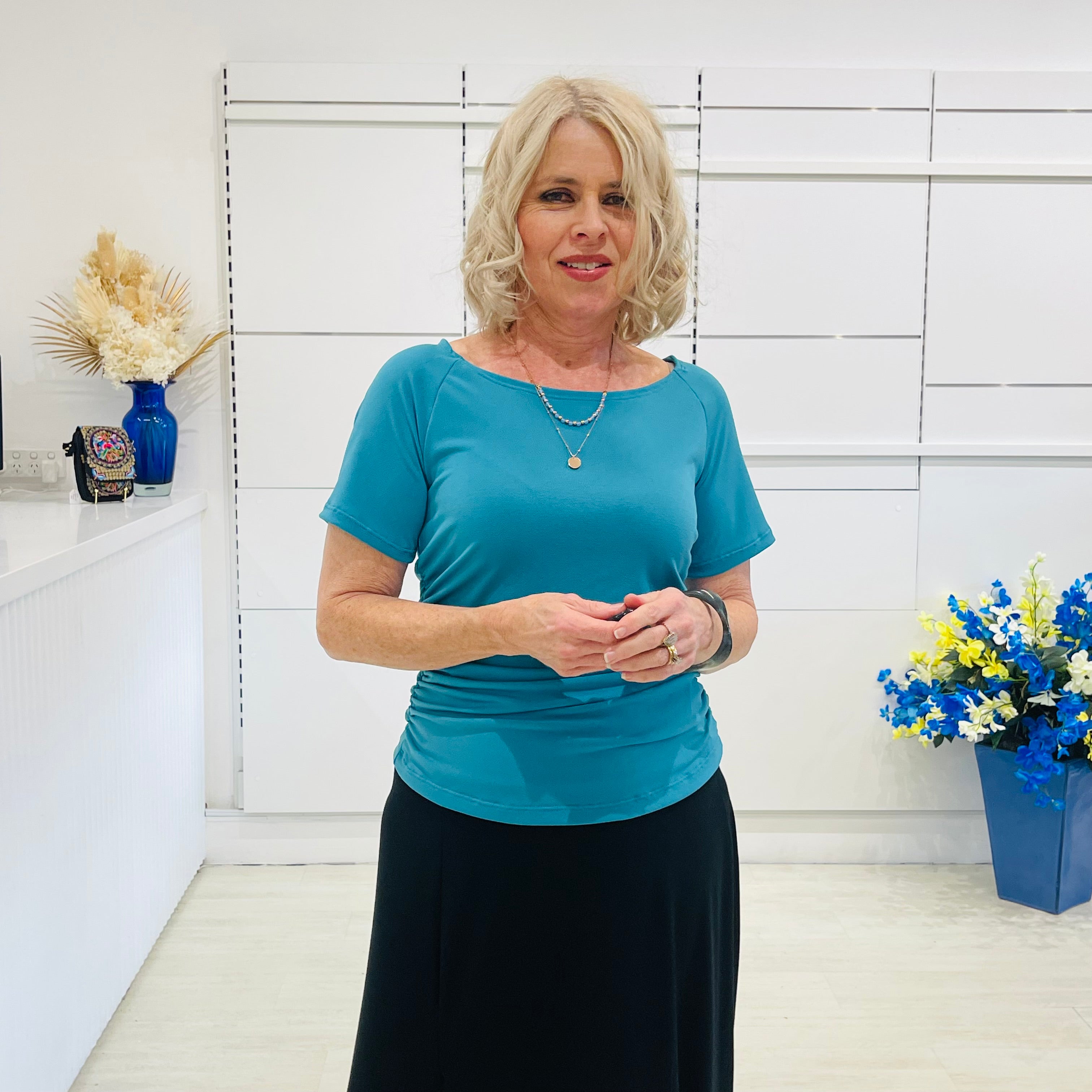 Woman in a green dressy top standing in a room with white walls and decorative elements.