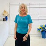Woman in a green dressy top standing in a room with white walls and decorative elements.