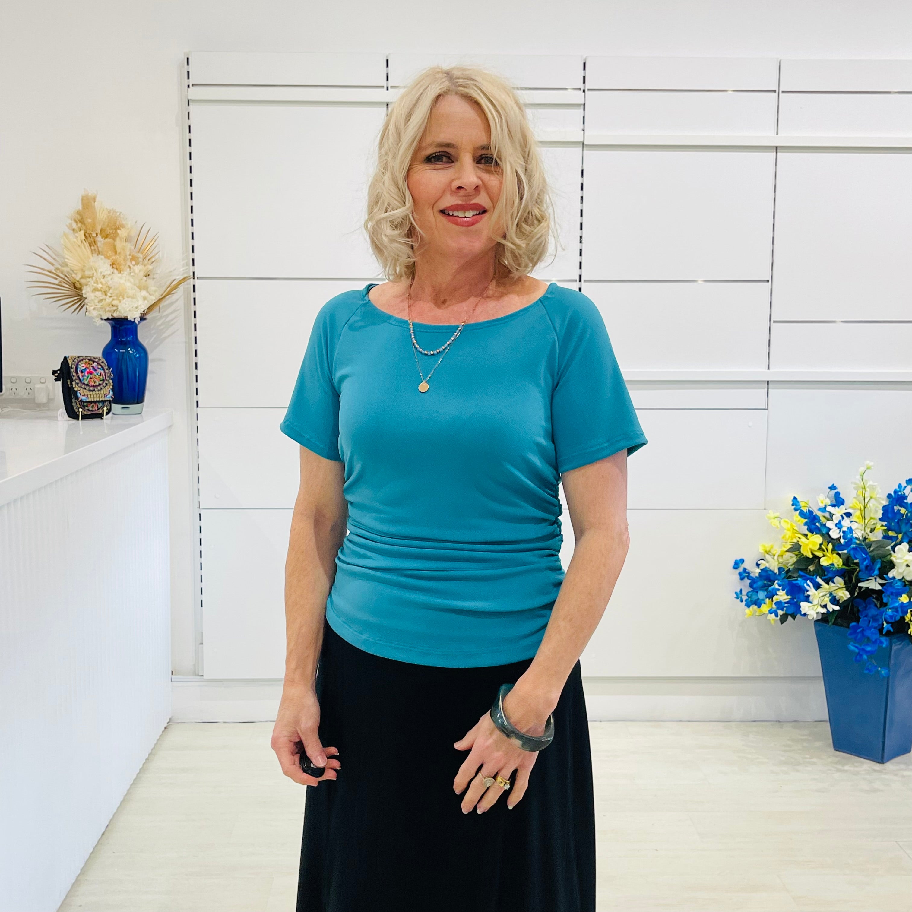 Woman in a green dressy top standing in a room with white walls and decorative elements.