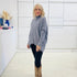 Grey knit sweater with long sleeves, high neckline and asymmetrical hemline. With black pants and brown embroidered boots.