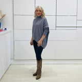 Grey knit sweater with long sleeves, high neckline and asymmetrical hemline. With black pants and brown embroidered boots.