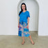 Woman wearing a blue top and colorful patterned skirt standing in front of a white wall with an arch.