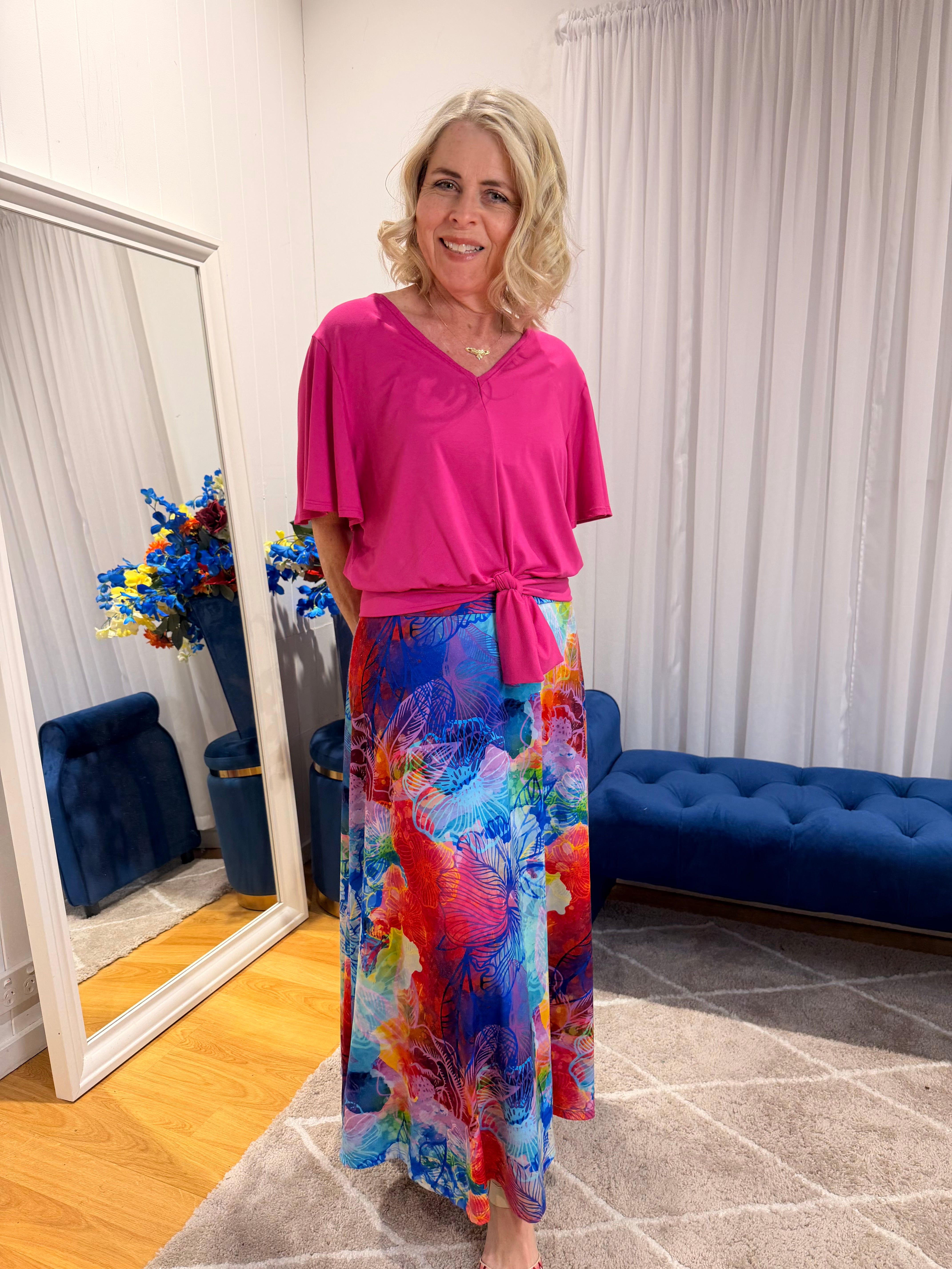 Woman wearing pink short sleeve top and colourful skirt.