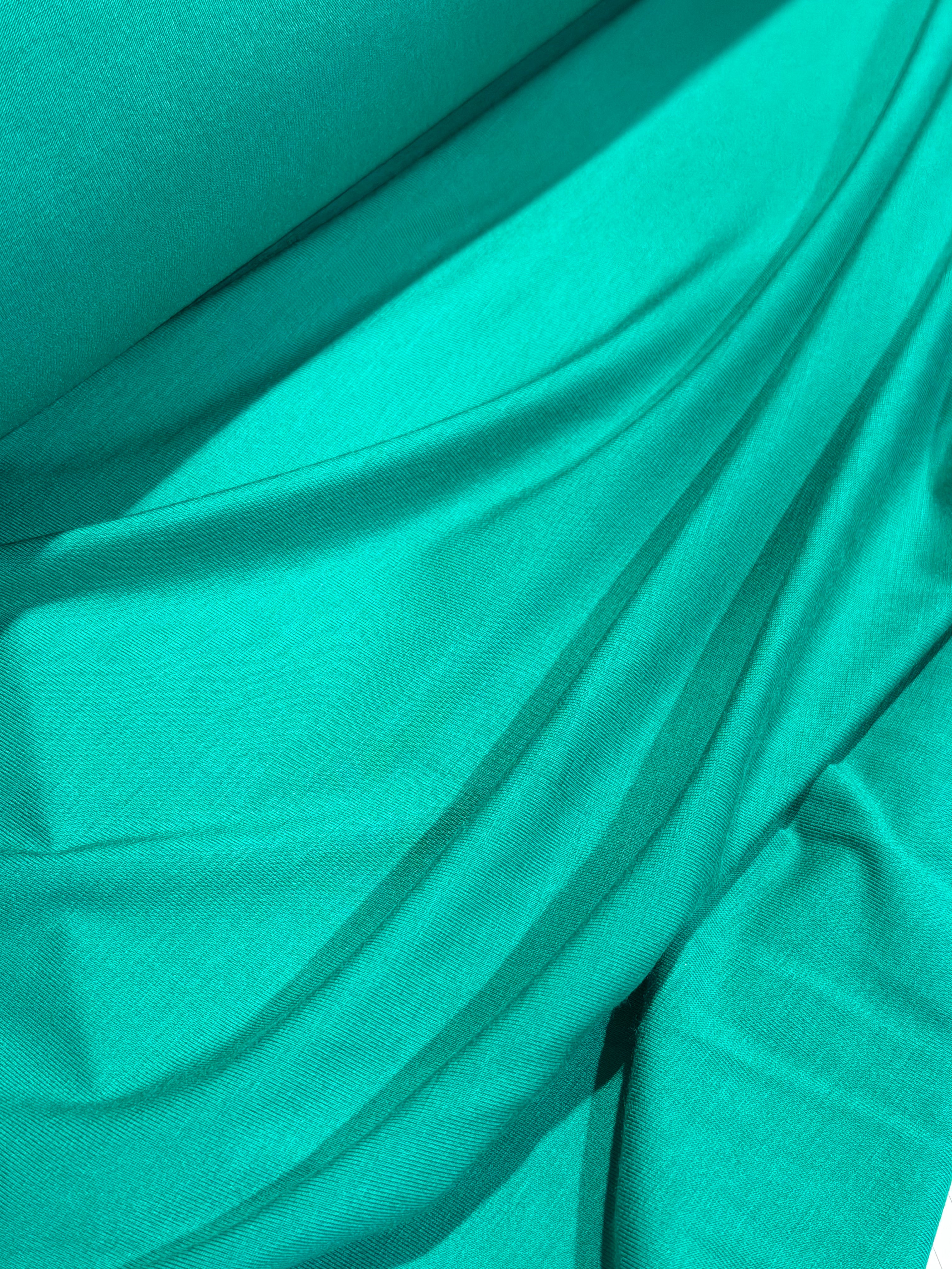 A close-up of draped teal fabric with soft folds and a smooth texture.